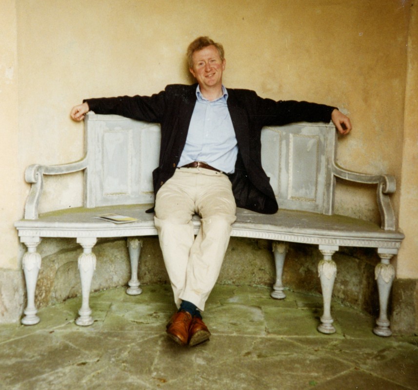 Giles Waterfield sat on a wooden bench in a relaxed manner 